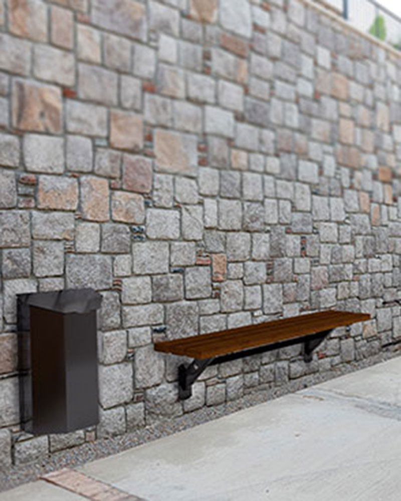 Image rendue d'un mur en pavés sur lequel sont fixés un banc public, un porte-vélos et une poubelle. Il s'agit d'un mobilier peu encombrant pour les environnements extérieurs.